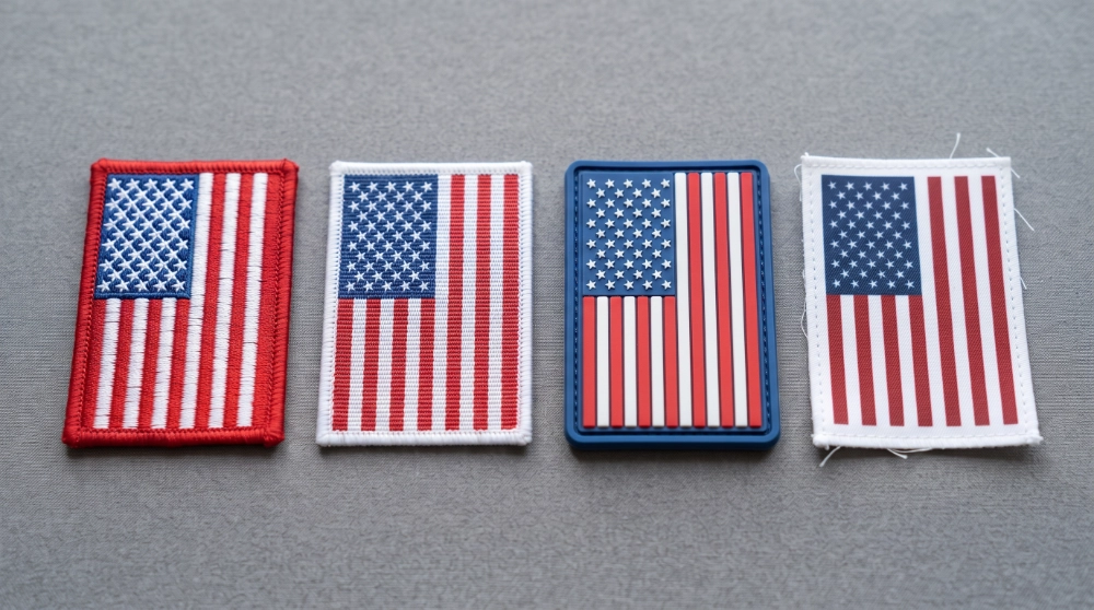 Four American flag patches side by side comparing embroidered, woven, PVC, and printed materials