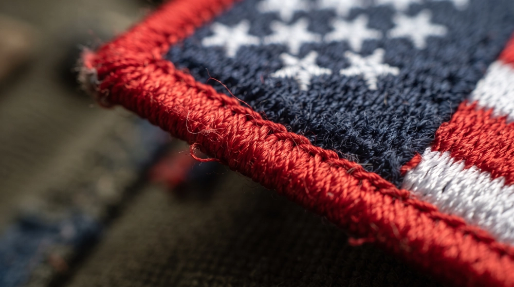 Flat-lay of a jacket, backpack, cap, and motorcycle vest each showing correct American flag patch placement