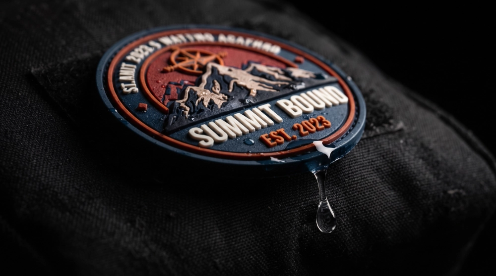 Close-up of a raised multi-color PVC patch with a mountain design and a water droplet dripping off its edge on dark fabric